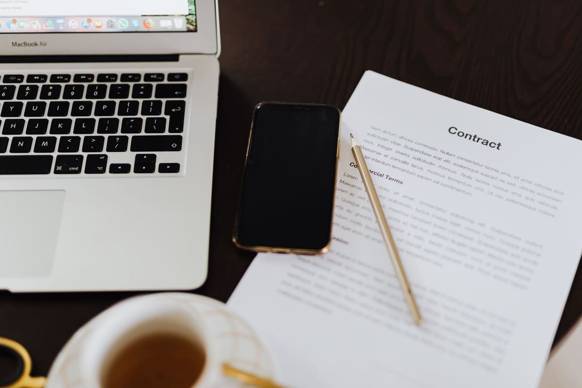 A printed contract, pen, phone and laptop on a desk